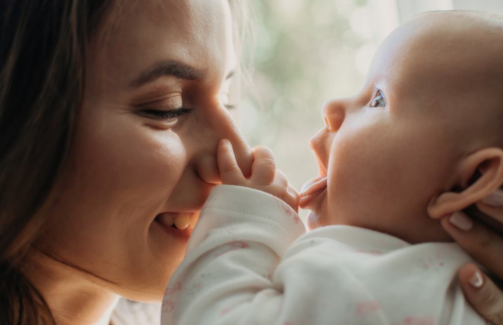 White woman and her baby having a tender moment in front of a window