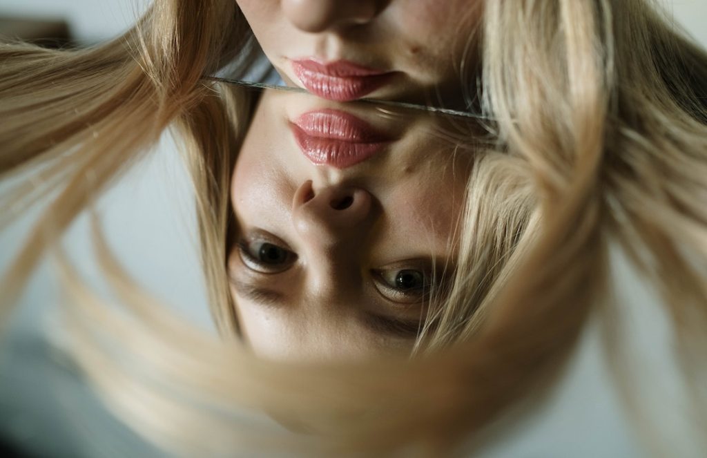 Blonde woman staring worriedly into her own reflection