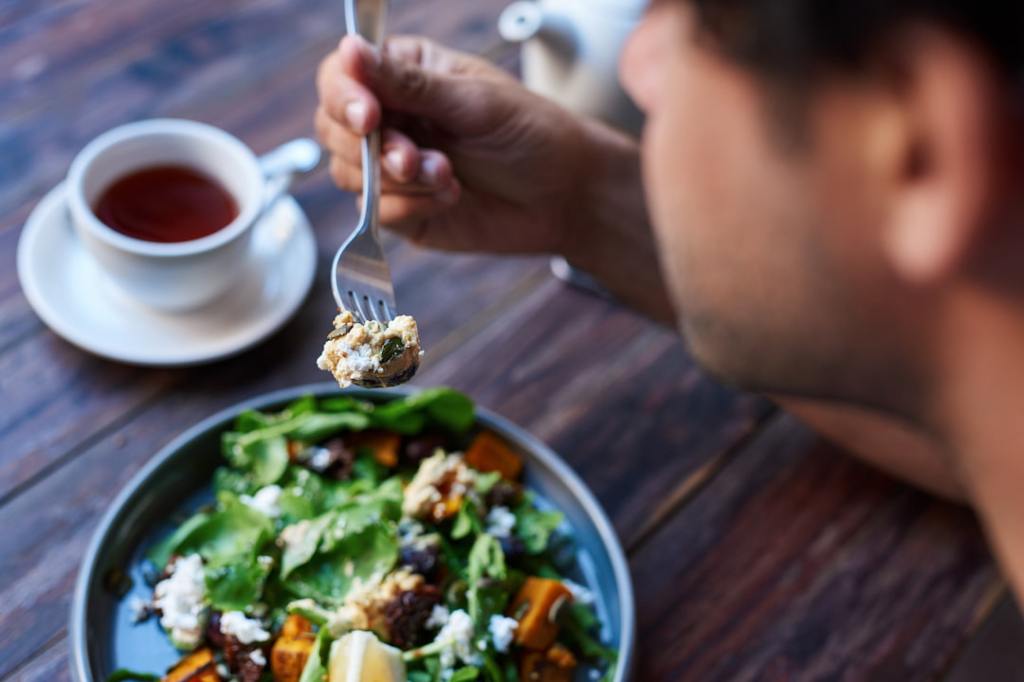 Person eating salad with coffee at a table