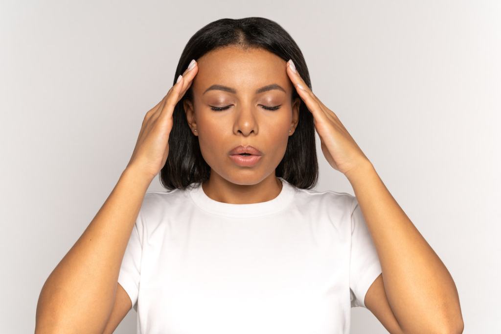 Woman in a white t-shirt rubbing her temples to relieve stress in front of white background