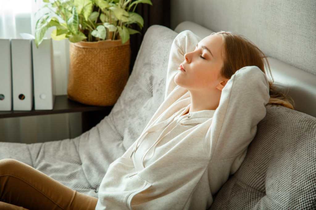 White woman laying on a couch in a white sweatshirt with her eyes closed