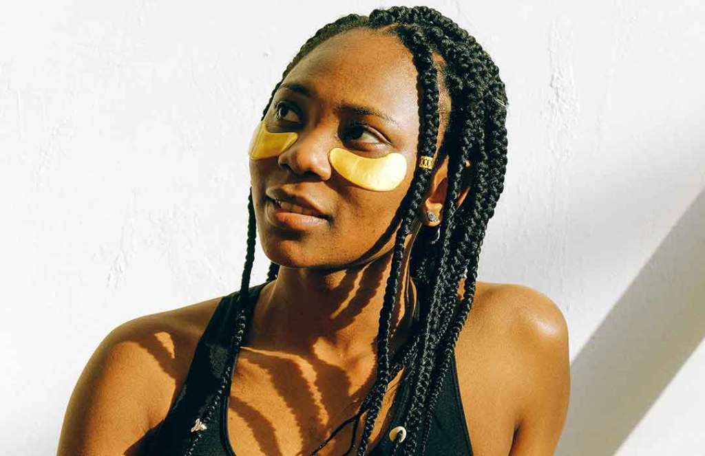 black woman with braids smiling with eye patches and black tank top