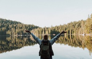 woman with arms up in front of lake