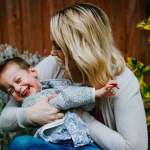blonde woman in grey sweater holding child in grey shirt