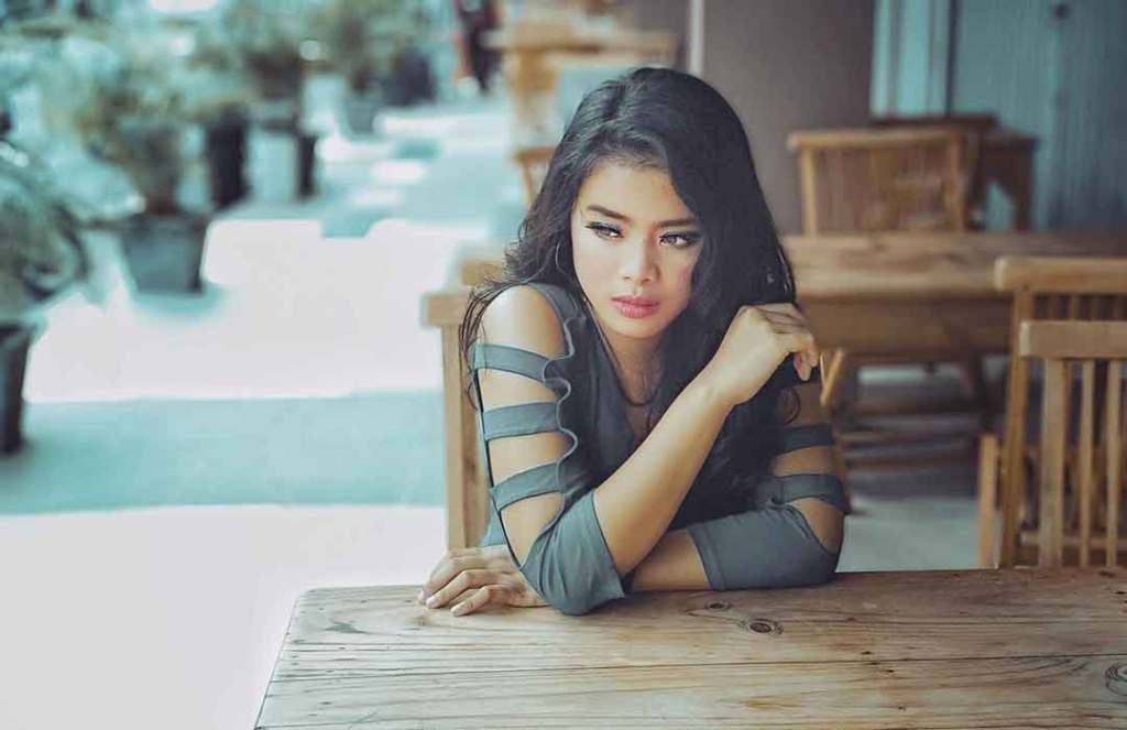 asian woman with dark hair in grey strappy long shirt sitting at wood table