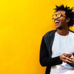 Man with sunglasses laughing against a yellow wall