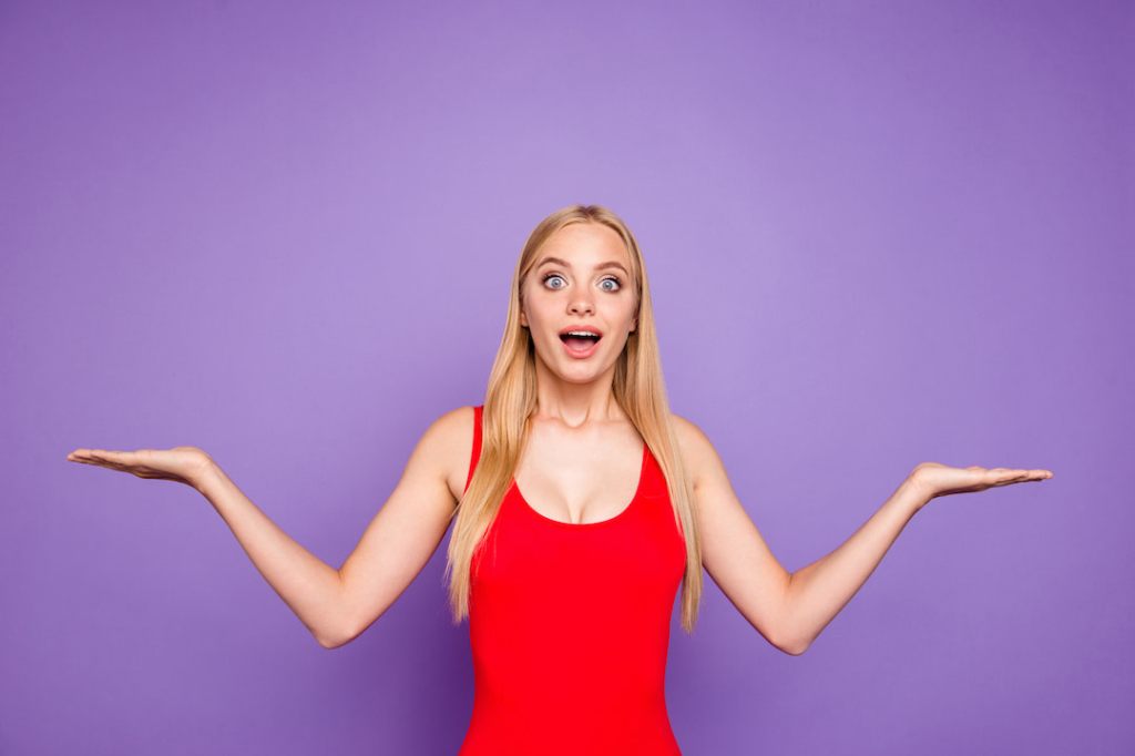 Happy woman in a red tank top making a funny pose in front of a purple background