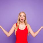 Happy woman in a red tank top making a funny pose in front of a purple background