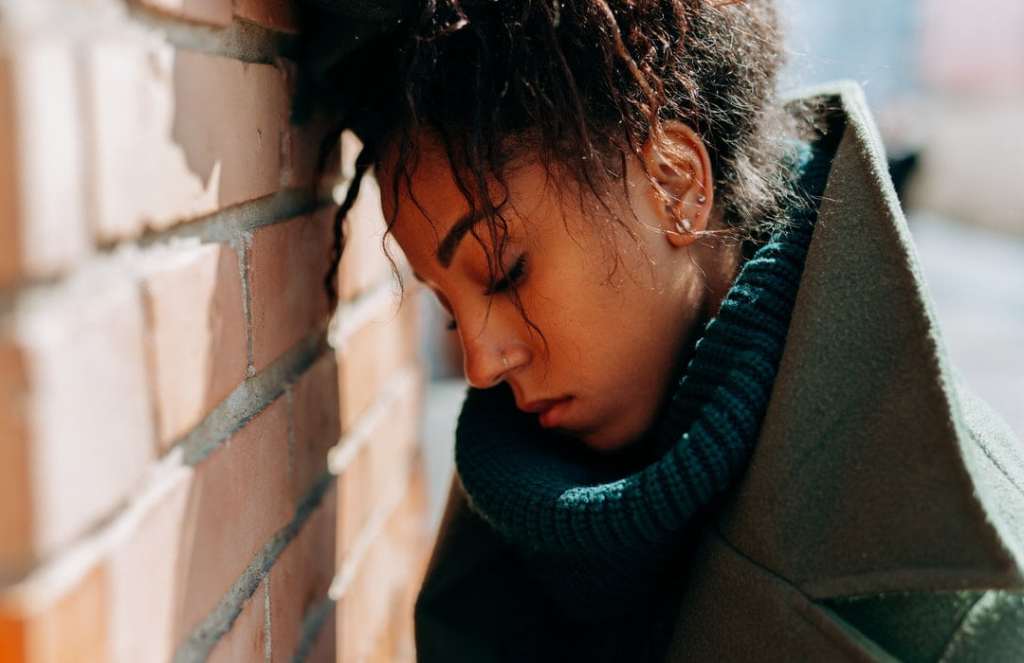 Sad woman with nose ring leans head against brick wall