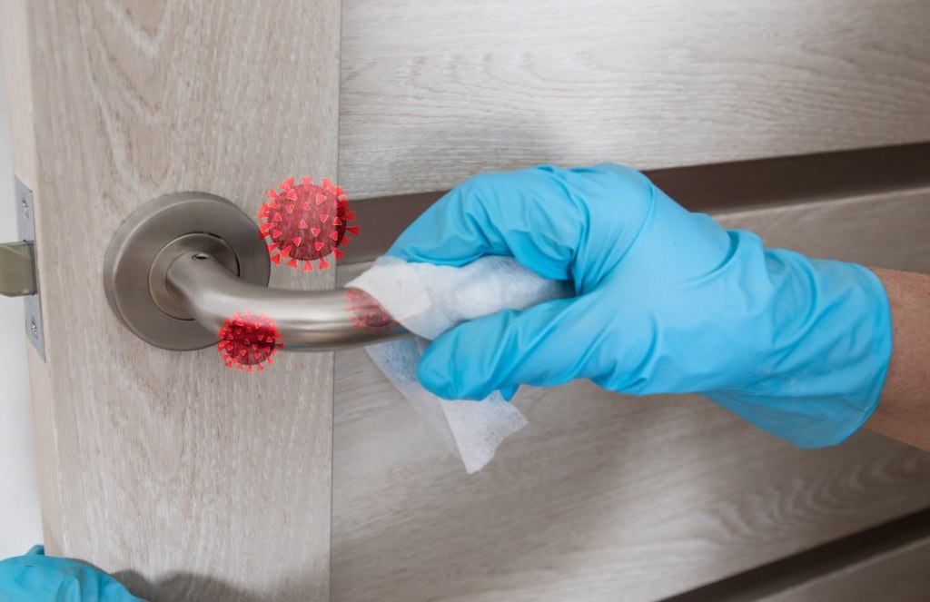 Person disinfecting a door handle with blue latex gloves and a disinfecting wipe