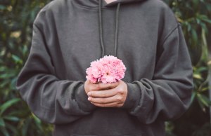 man in grey sweatshirt holding pink flower