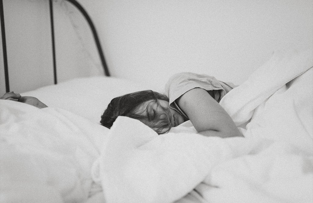 Tired young woman sleeping well on the side in bed with white sheets,  resting after sleepless