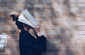 woman holding book against head on brick wall