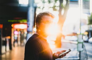 man holding phone on street with bright sun