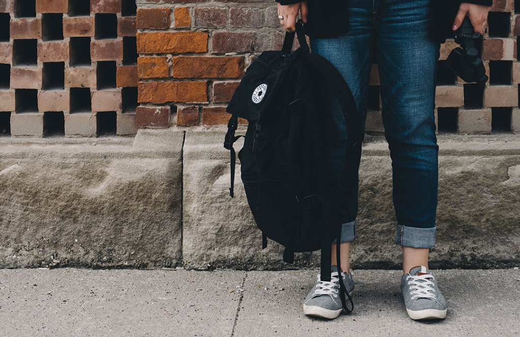 person in jeans standing with black backpack