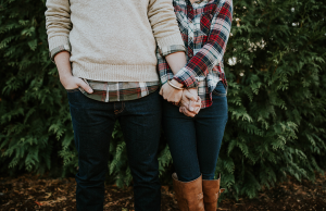 Couple wearing plaid holding hands in front of greenery