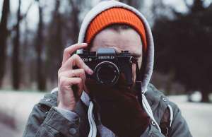 man in orange and green hoodie taking picture with black camera
