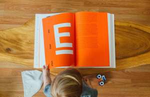 child reading orange book with letter e