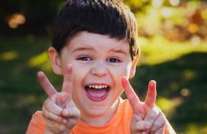 child in orange t-shirt holding peace sign