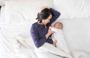woman laying on white bed with baby