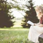 woman in white skirt reading book in grass