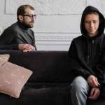 man and teenager in dark clothes on couch