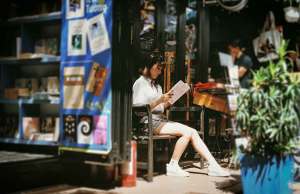 girl in white shirt reaching a book outside on the patio of a bookstore