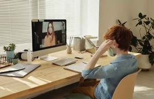 red haired child in blue shirt and mask on video chat with a woman in a mask
