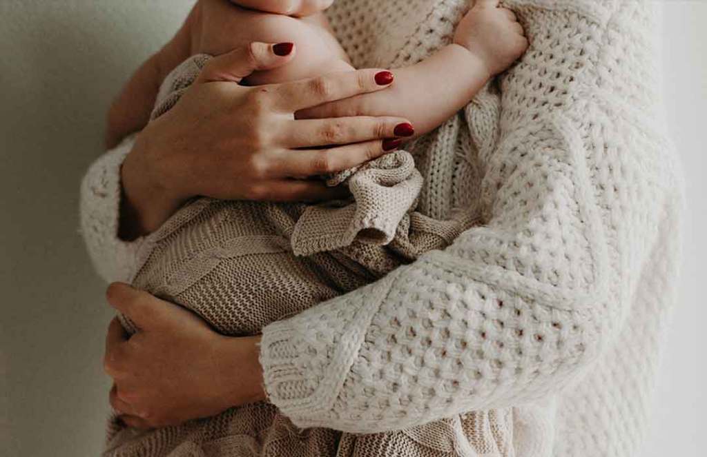 woman in white knit sweater holding baby in white blanket