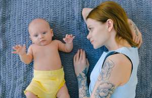 woman with tattoos laying on blue mat with baby in yellow diaper