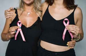 two woman in black shirts holding pink breast cancer awareness ribbons
