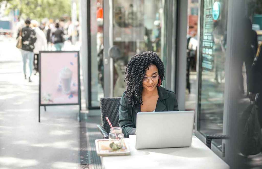 woman with black curly hair in black blazer working outside on laptop