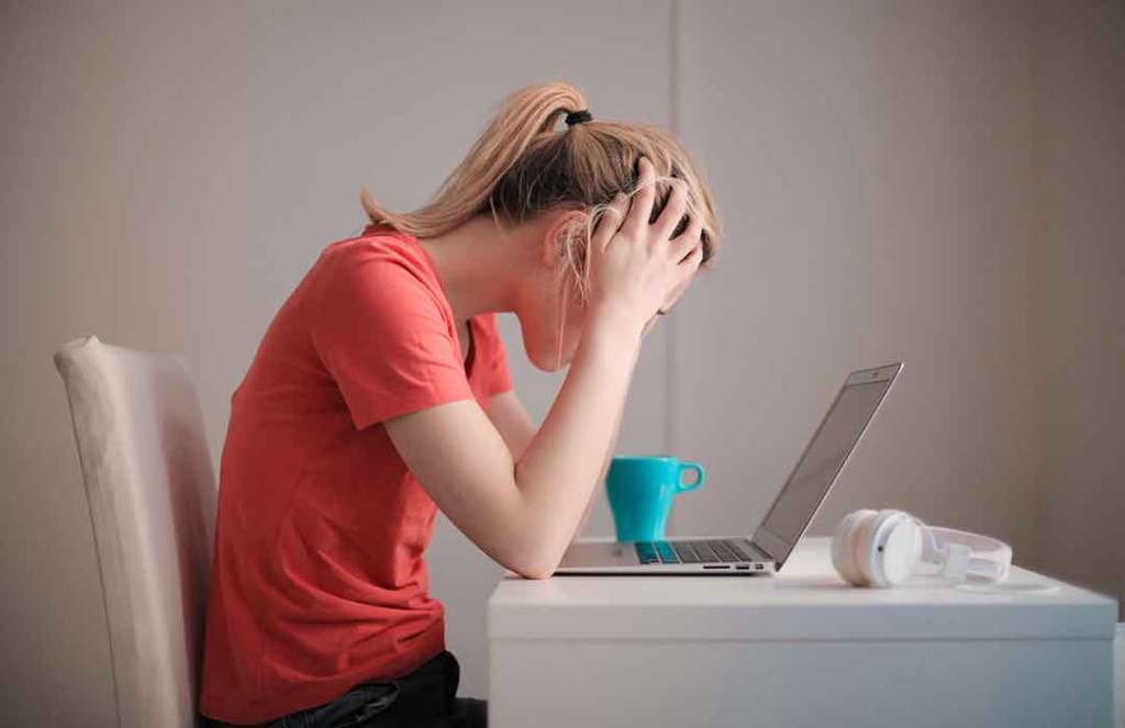 woman in pink shirt holding head by laptop and teal mug