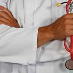 Man in white lab coat holding red stethoscope