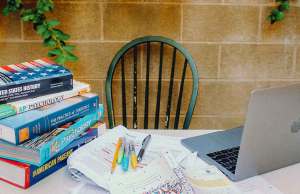 black wooden chair in front of stone wall with table, books and a laptop