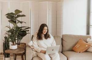 woman in white oufit sitting on grey couch using apple laptop