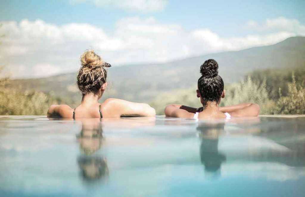 two girls in blue water looking out into mountain landscape