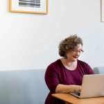 woman in red shirt sitting at table on laptop