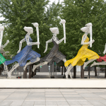 five running women wearing different colored dresses holding Olympic torches