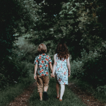 two children holding hands, walking on a path through the woods