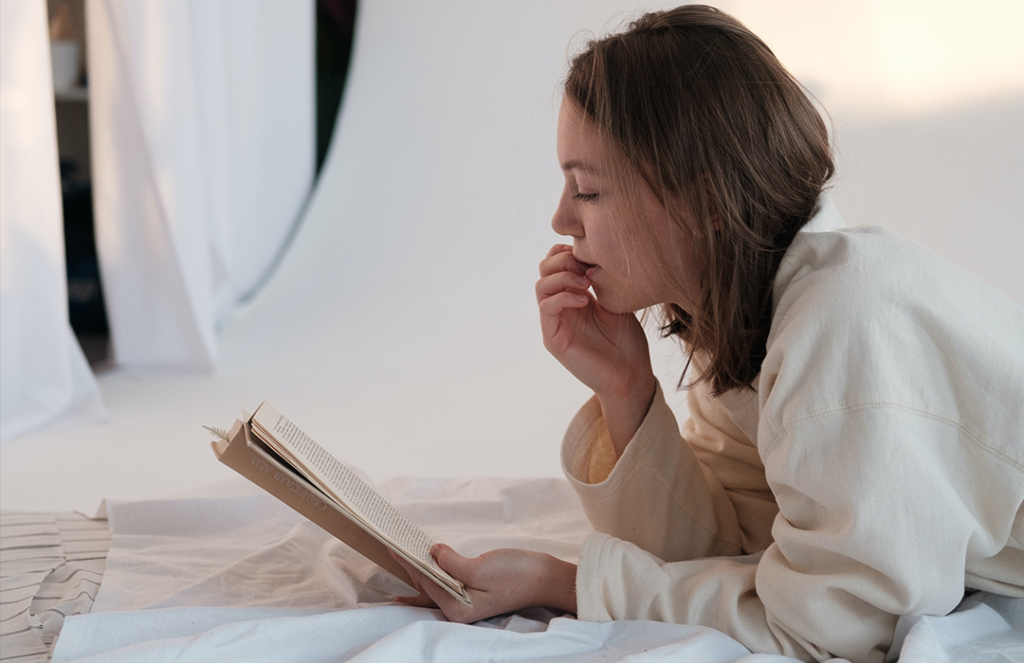 young female in white shirt laying down reading book
