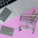 silver shopping cart with silver credit cards and silver macbook computer