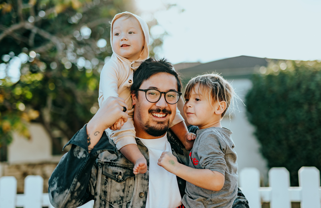 man in white shirt and glasses carrying two kids