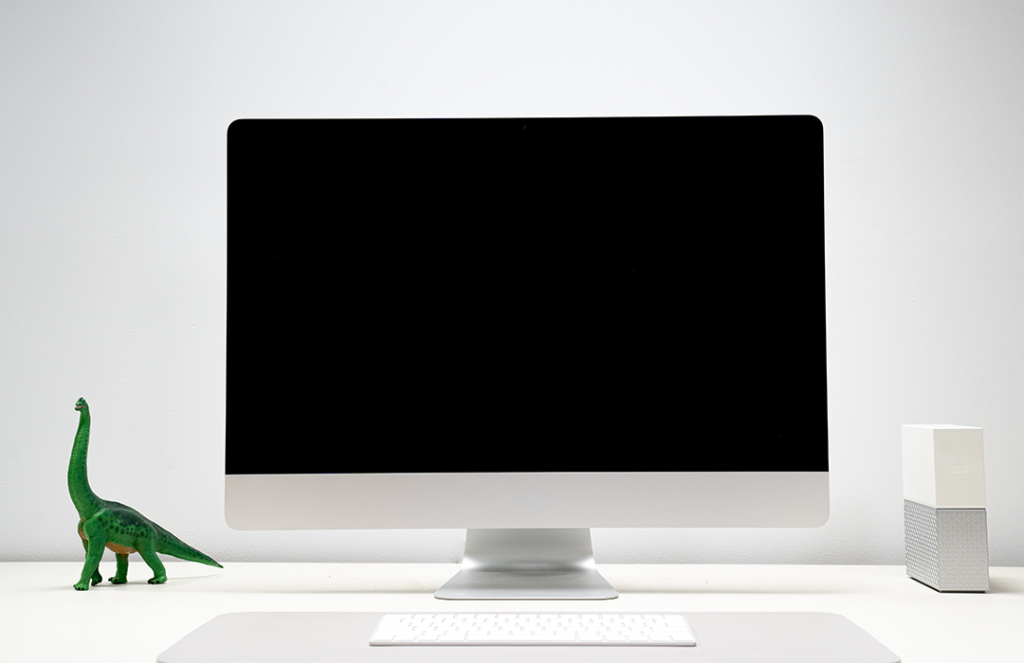 black and white desktop computer with green brontosaurus sitting on desk