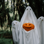 three ghosts holding carved pumpkin
