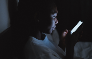 woman in white shirt sitting in dark room using phone