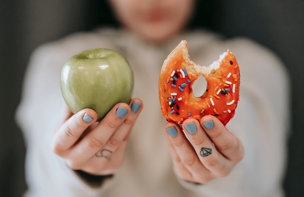 woman holding apple in one hand and bitten doughnut in other