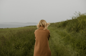 A blonde woman in brown coat walks alone in a field