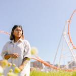 Woman in white shirt poses with flowers in front of roller coaster