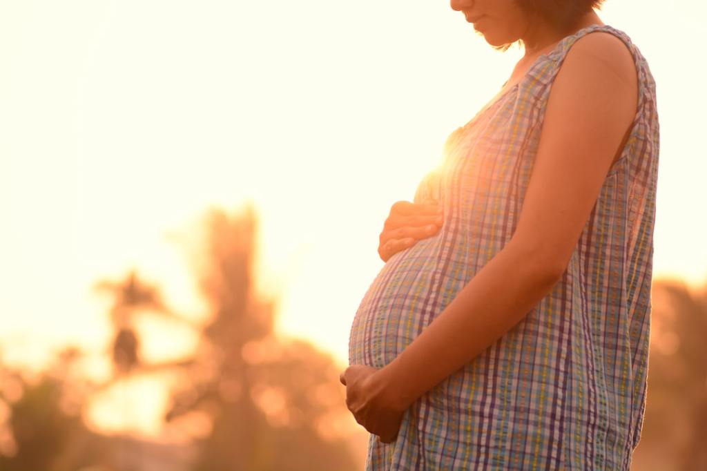 A pregnant woman holding her belly at sunset